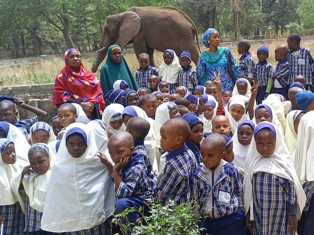 Pupils and their teachers on a school trip to the zoo, with an elephant behind them